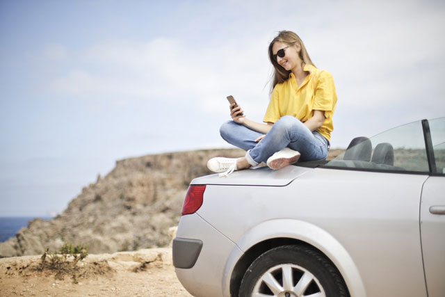 Girl on the beach with her car and phone