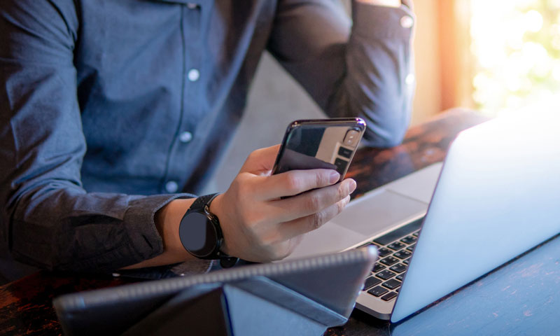 Man looking at his phone next to his laptop on a table