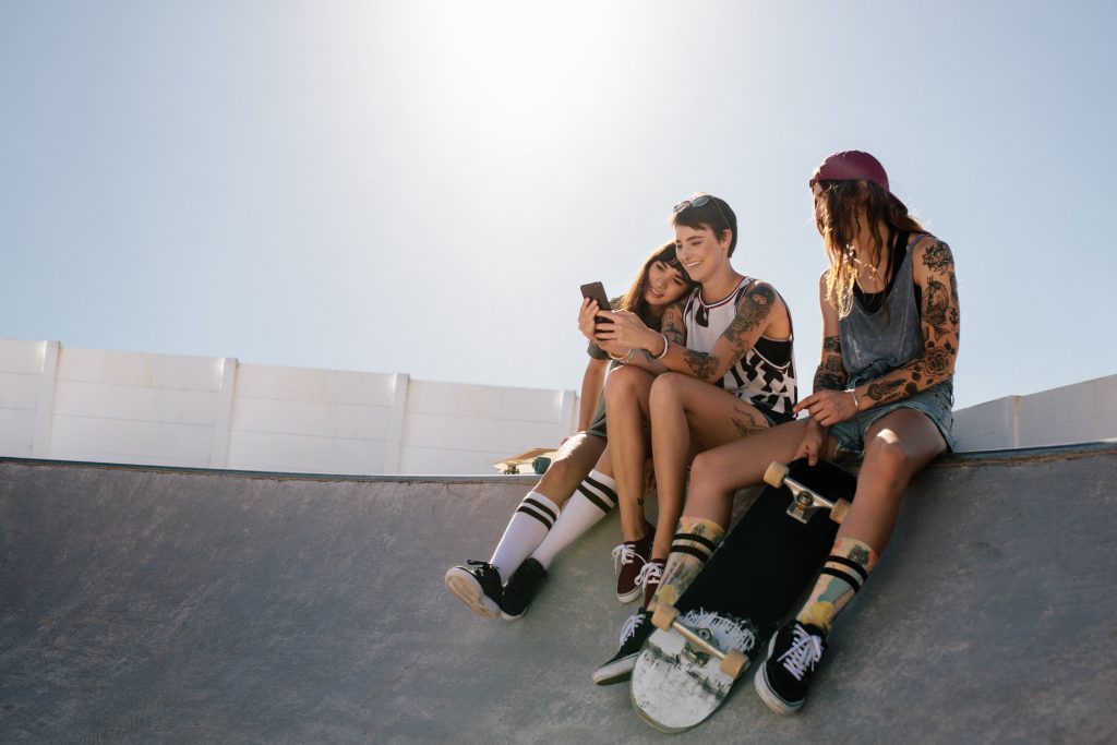 Girls looking at their phone sitting on a skateboard ramp with their skateboards