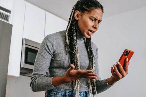 Woman in kitchen looking at her phone frustrated